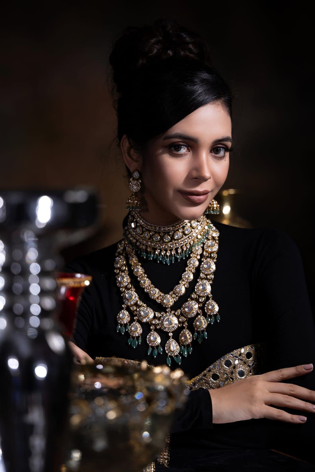 Woman in a black turtleneck layered with polki and emerald necklaces