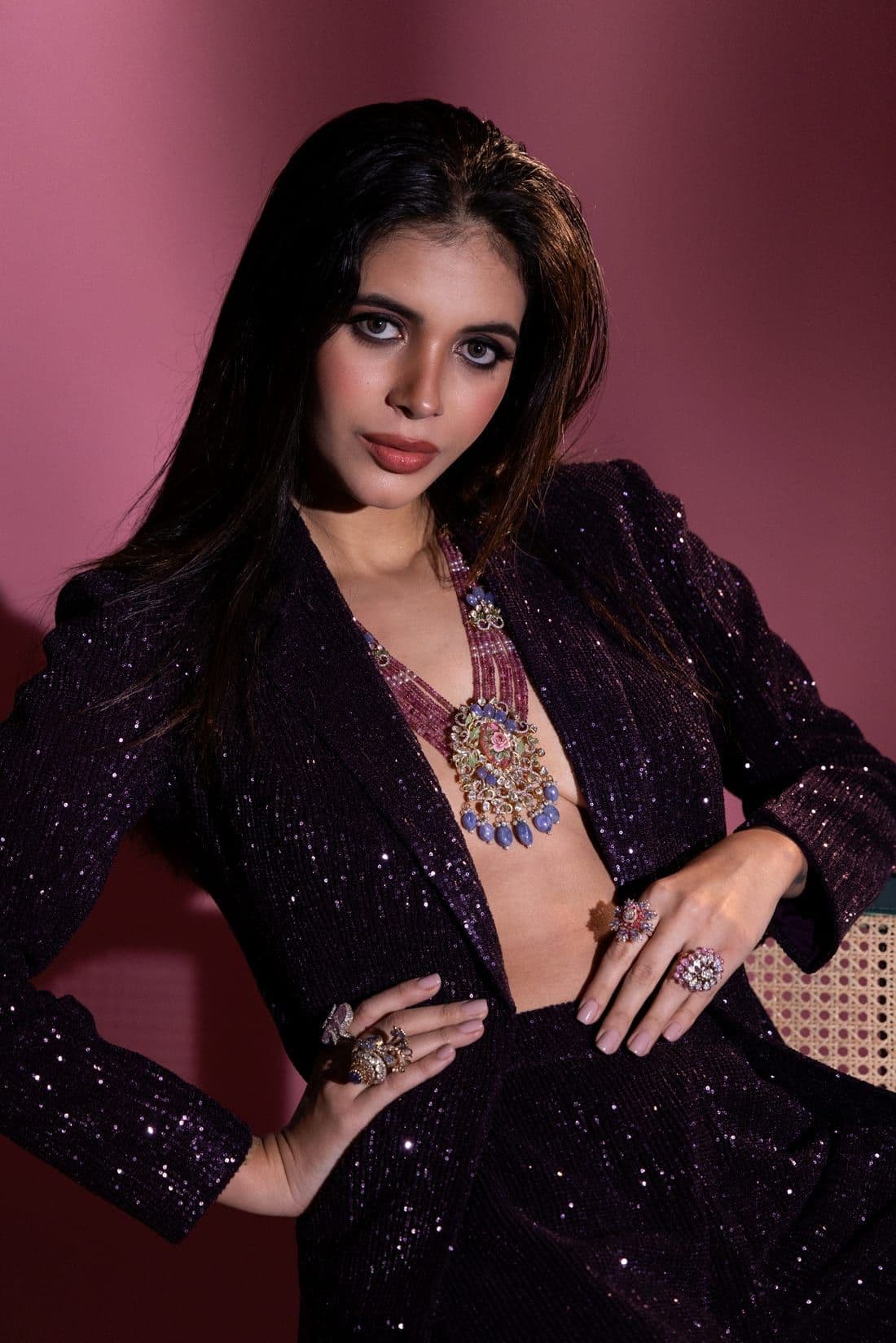 Woman in a plum sequin blazer with a beaded necklace and cocktail rings