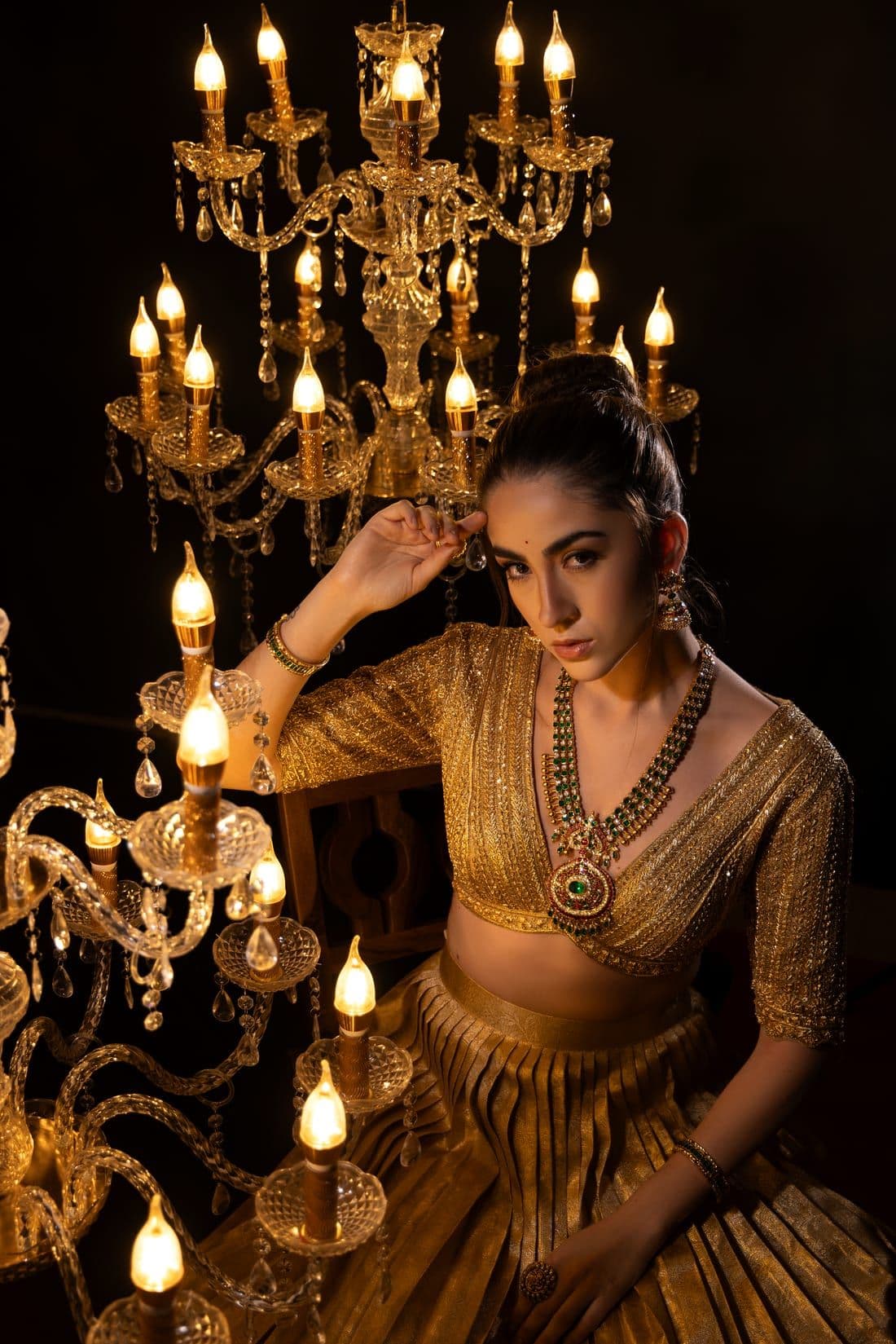 Woman in a gold lehenga seated among lit crystal chandeliers