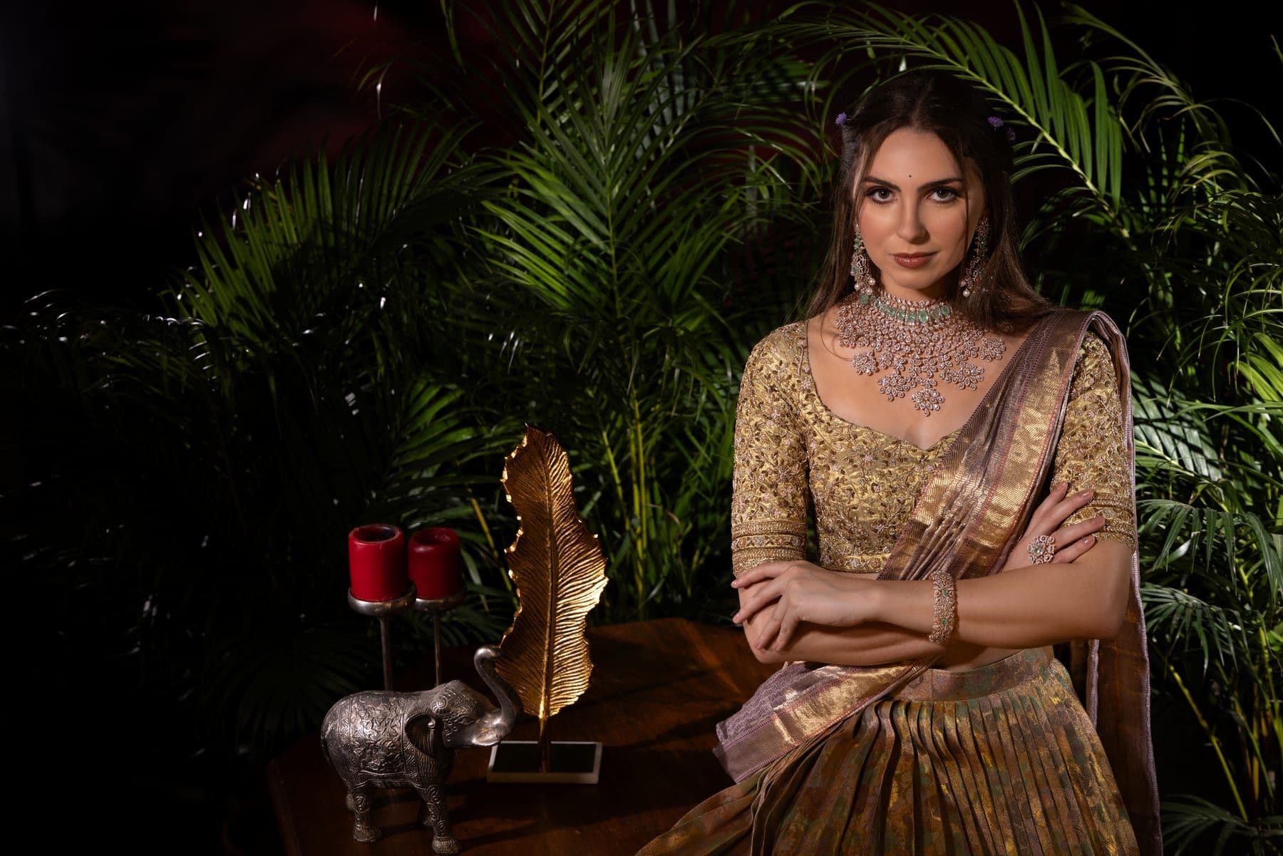 Woman in a gold tissue lehenga and diamond necklace among palm fronds