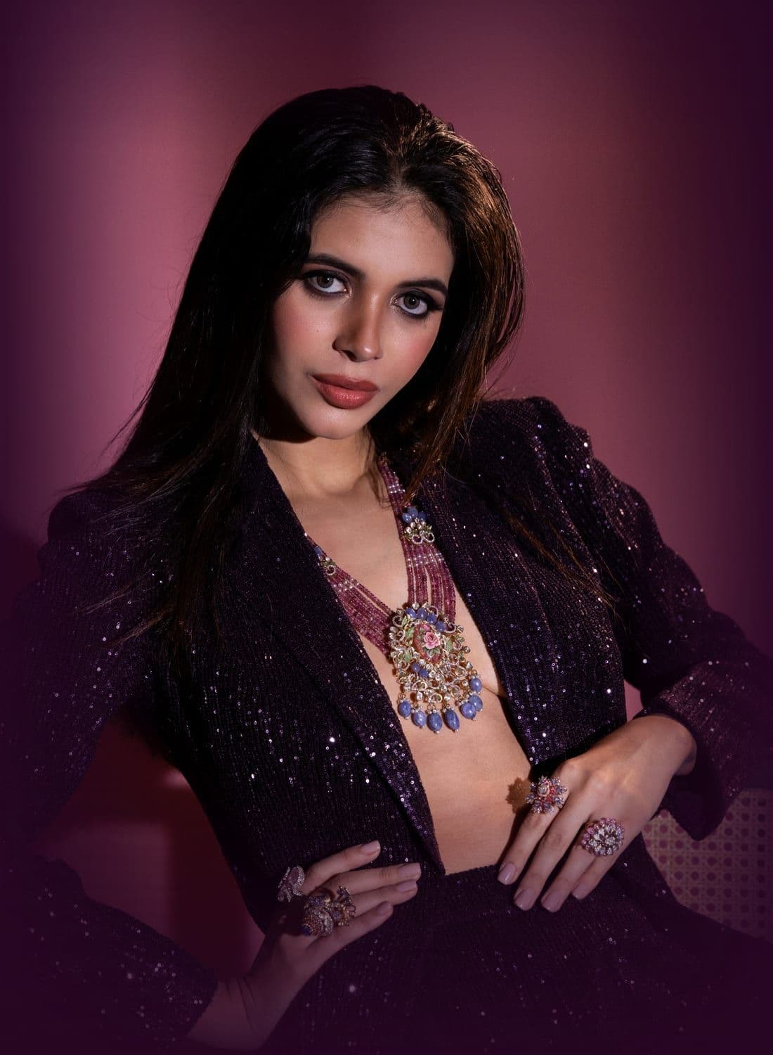 Woman in a plum sequin blazer with a beaded necklace and cocktail rings